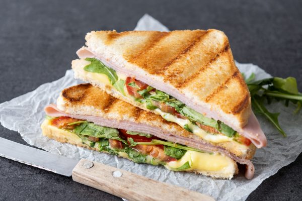 Panini sandwich with ham, cheese, tomato and arugula on black slate background